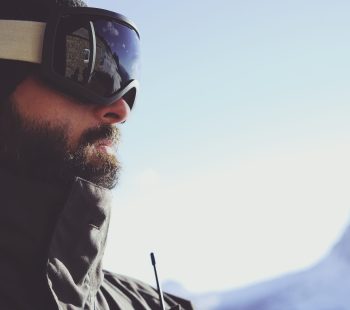 Close-up portrait of bearded young snowboarded in sunglass mask, at the ski resort